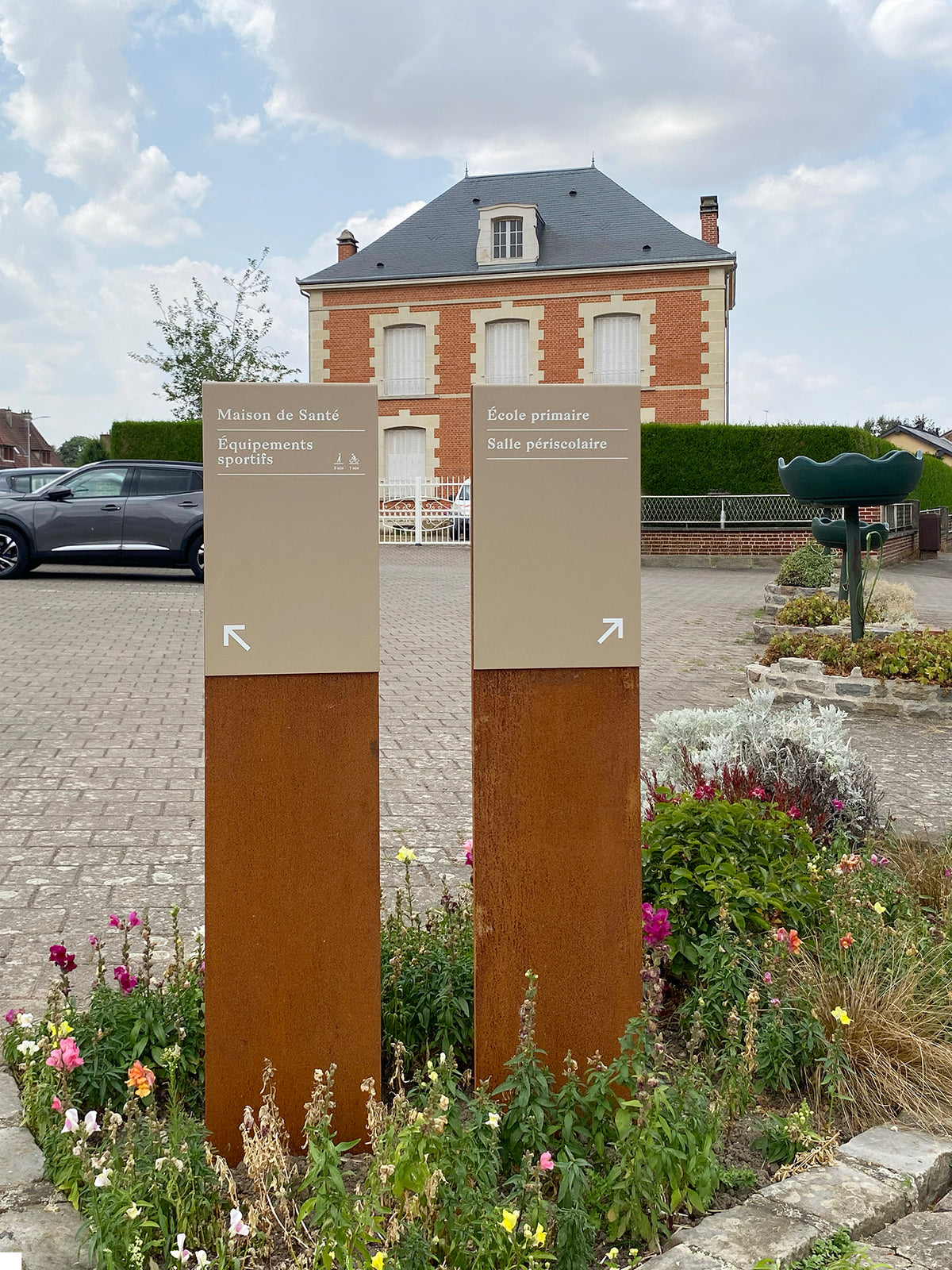 Double totem de jalonnement directionnel piéton, sur parterre fleuri