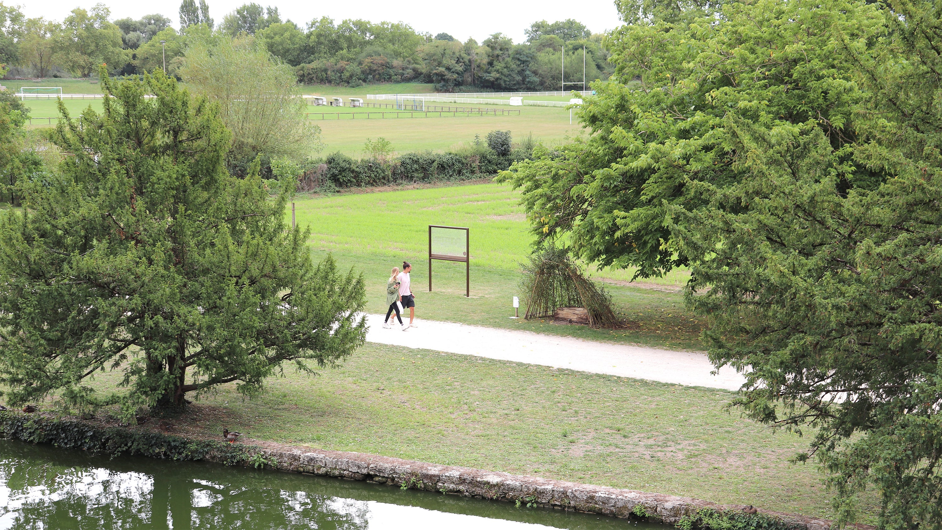 Dispositif immersif au bord de l’eau intégré à un parc paysager avec parcours piéton dans un environnement historique